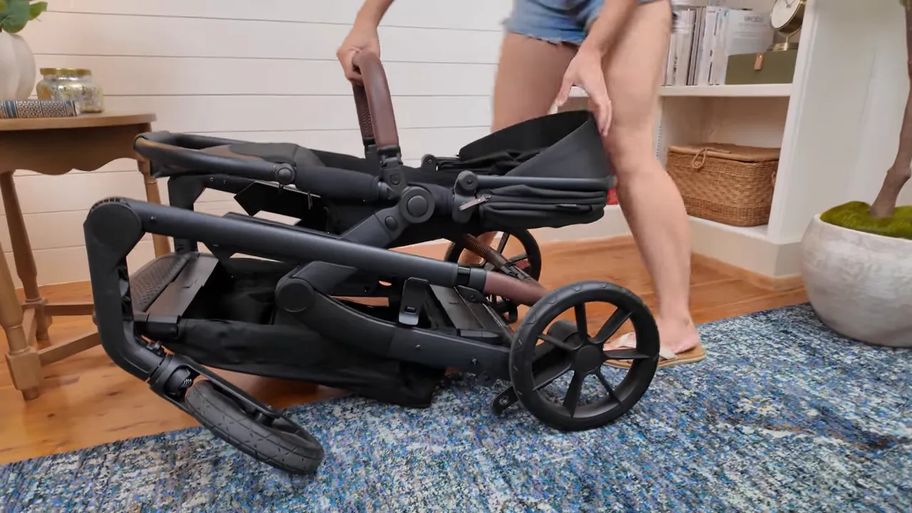 Folding the Momcozy ChangeGo, stroller mid-fold with handlebar lowered
